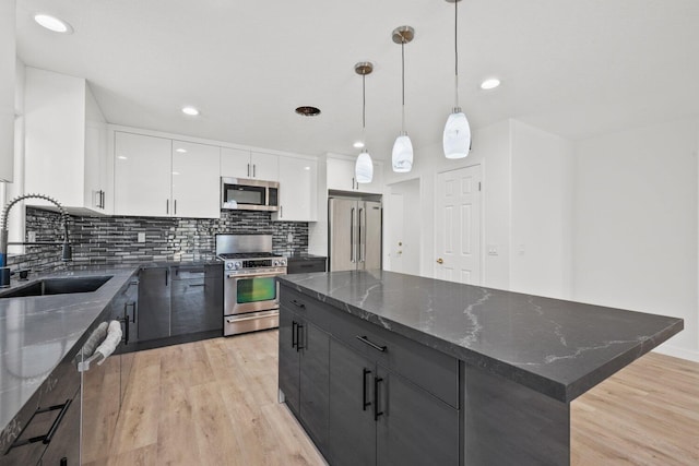 kitchen with appliances with stainless steel finishes, a center island, a sink, light wood finished floors, and white cabinetry