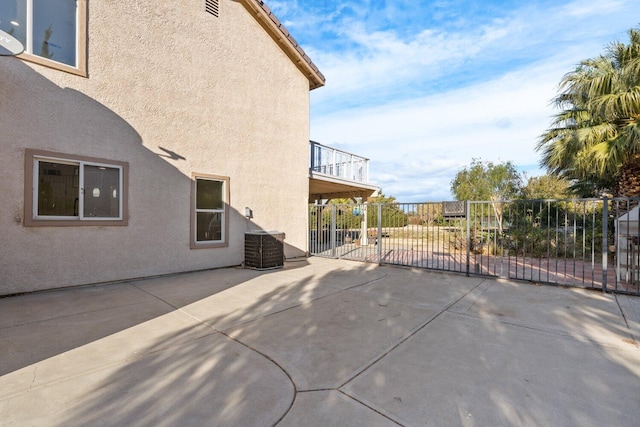 view of patio with central air condition unit, fence, and a balcony