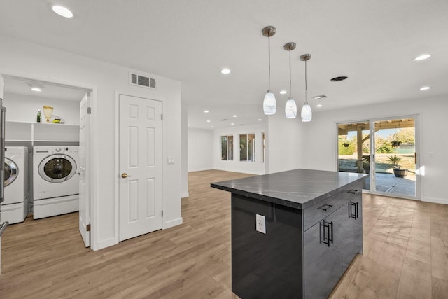 kitchen with light wood-style floors, dark countertops, visible vents, and washer and clothes dryer