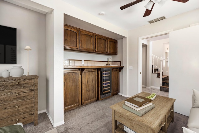 bar with light carpet, beverage cooler, and ceiling fan