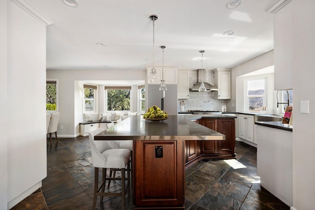 kitchen featuring wall chimney exhaust hood, sink, a breakfast bar area, hanging light fixtures, and a kitchen island