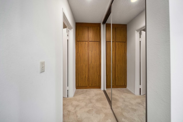 hallway with light carpet and a textured ceiling