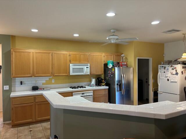 kitchen with tile countertops, ceiling fan, white appliances, and light brown cabinetry