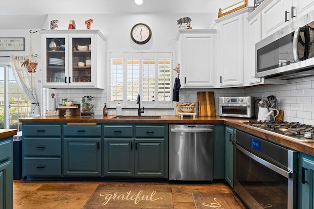 kitchen featuring stainless steel appliances, a sink, white cabinetry, butcher block countertops, and tasteful backsplash