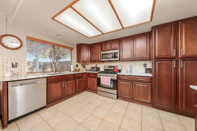 kitchen with sink, decorative backsplash, light stone countertops, light tile patterned floors, and stainless steel appliances