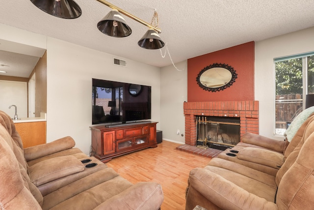 living room with light hardwood / wood-style floors, a textured ceiling, and a brick fireplace