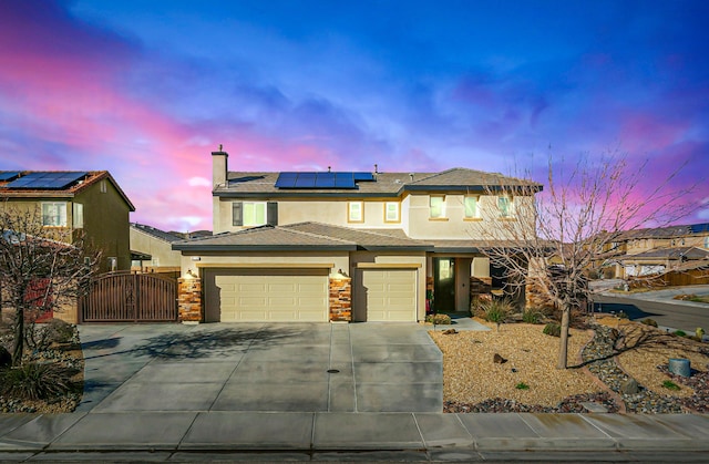 view of front of home with a garage, driveway, roof mounted solar panels, a gate, and stucco siding