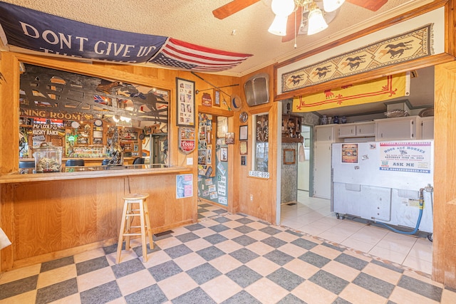 interior space featuring wood walls, ceiling fan, ornamental molding, a kitchen bar, and kitchen peninsula