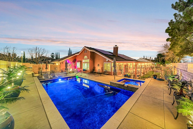 pool at dusk with a patio area and an in ground hot tub