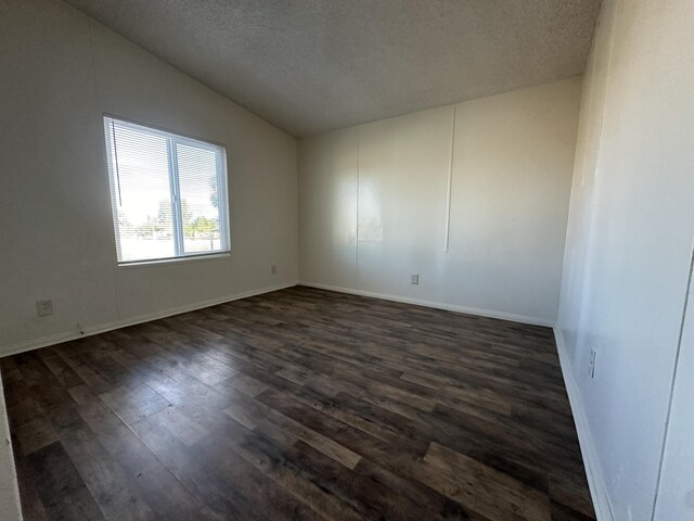 empty room with a textured ceiling, dark wood-type flooring, and vaulted ceiling