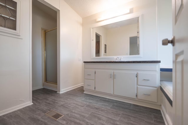 bathroom with a textured ceiling, vanity, walk in shower, and wood-type flooring