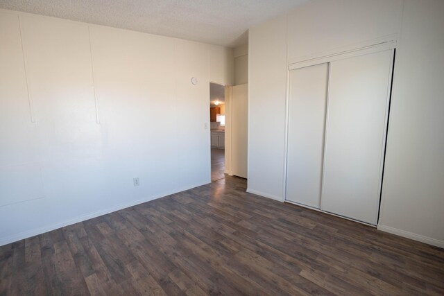 unfurnished bedroom with a textured ceiling, dark hardwood / wood-style floors, and a closet