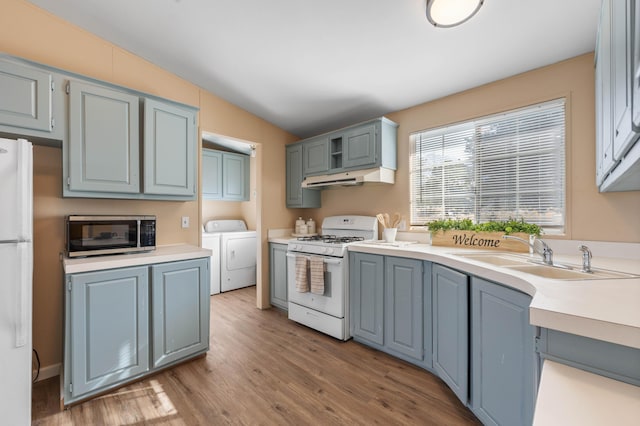 kitchen with vaulted ceiling, sink, independent washer and dryer, light hardwood / wood-style floors, and white appliances