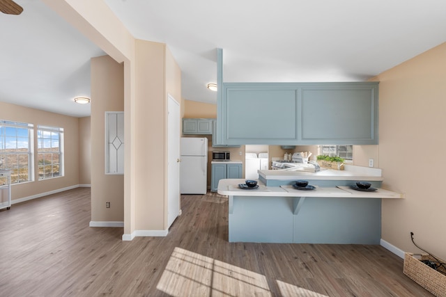 kitchen featuring washer / dryer, a kitchen breakfast bar, kitchen peninsula, white fridge, and hardwood / wood-style floors