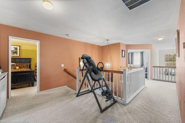 exercise area featuring light colored carpet and a textured ceiling