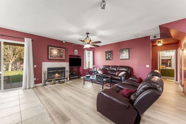 living room with ceiling fan, light wood-type flooring, and a tiled fireplace