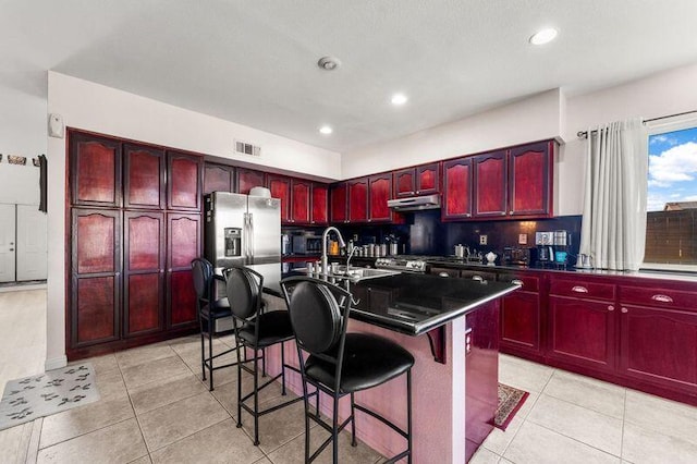 kitchen featuring sink, tasteful backsplash, stainless steel fridge, a breakfast bar area, and a center island with sink