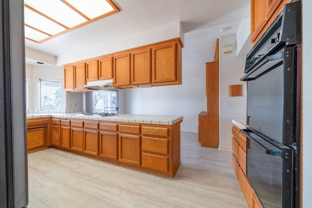 kitchen with kitchen peninsula, tile countertops, stainless steel gas cooktop, and double oven