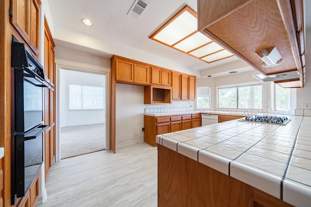 kitchen featuring white dishwasher, tile counters, kitchen peninsula, and stainless steel gas stovetop