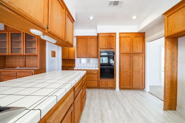 kitchen with double oven, tile countertops, light hardwood / wood-style flooring, and a textured ceiling