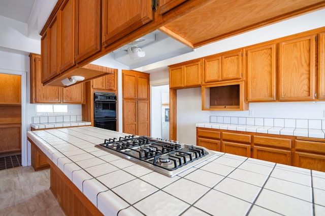 kitchen with tile countertops, black double oven, light hardwood / wood-style flooring, and stainless steel gas cooktop