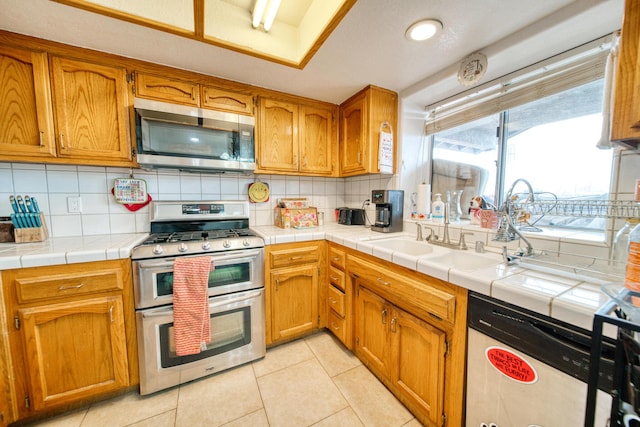 kitchen featuring light tile patterned flooring, stainless steel appliances, tasteful backsplash, a sink, and brown cabinetry