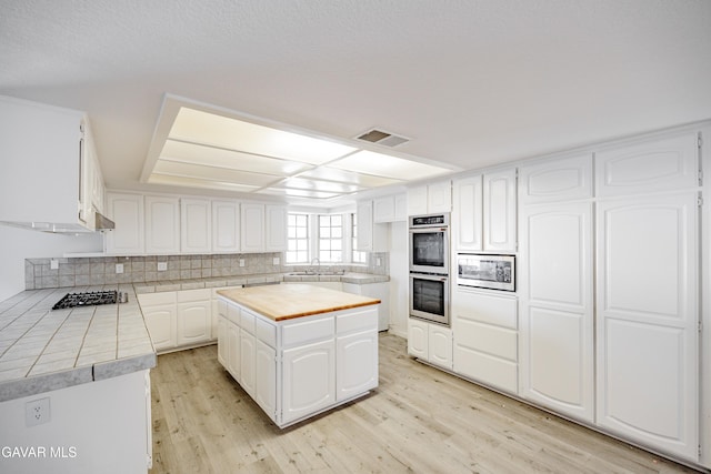 3807 Paula Ln, Lancaster, CA 93535 - kitchen featuring appliances with stainless steel finishes, light wood-style floors, backsplash, white cabinets, and tile countertops