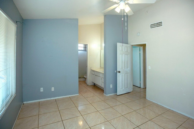 unfurnished bedroom with connected bathroom, a towering ceiling, ceiling fan, and light tile patterned flooring