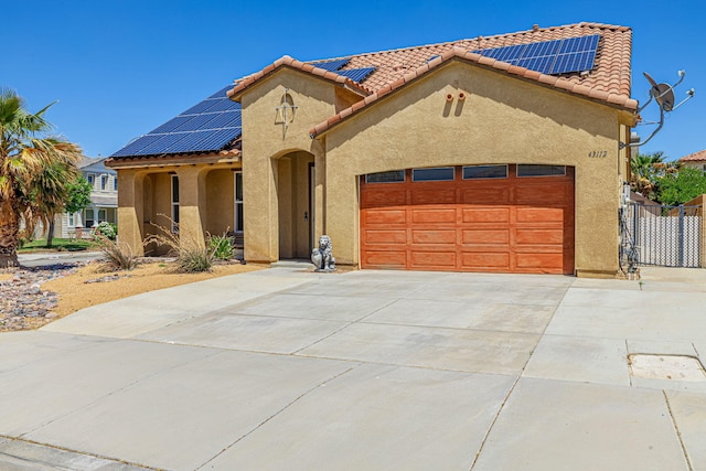 mediterranean / spanish house featuring stucco siding, solar panels, concrete driveway, and an attached garage
