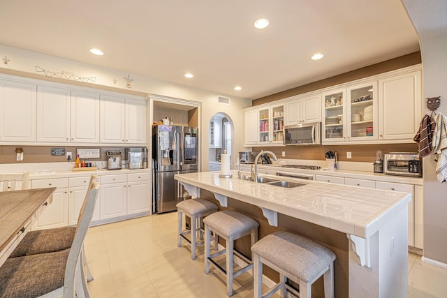 kitchen featuring stainless steel appliances, arched walkways, a sink, white cabinetry, and a breakfast bar