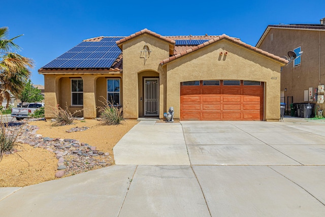 mediterranean / spanish-style home with roof mounted solar panels, concrete driveway, stucco siding, a garage, and a tiled roof