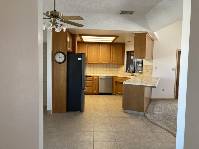 kitchen featuring black refrigerator, kitchen peninsula, stainless steel dishwasher, tile countertops, and lofted ceiling