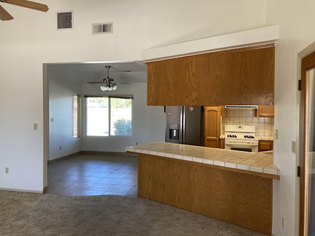 kitchen featuring stainless steel refrigerator with ice dispenser, white gas range oven, light colored carpet, ceiling fan, and tile countertops