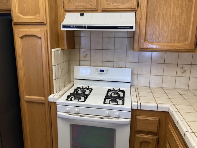 kitchen featuring black refrigerator, decorative backsplash, white gas stove, and tile counters