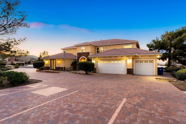 mediterranean / spanish-style home with a garage, a tile roof, stone siding, decorative driveway, and stucco siding