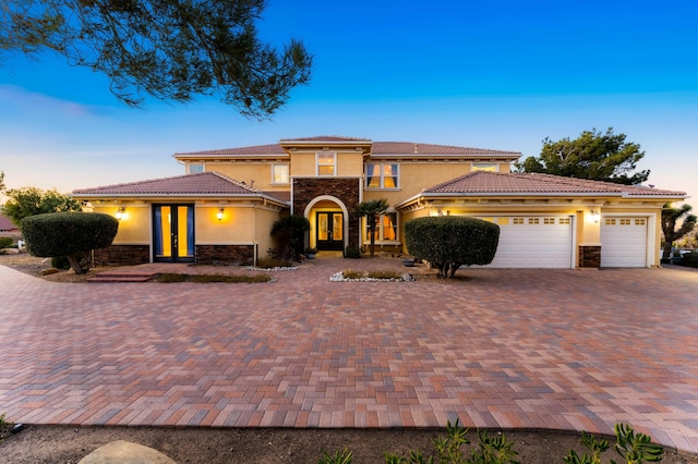 mediterranean / spanish house with a garage, stone siding, decorative driveway, and stucco siding