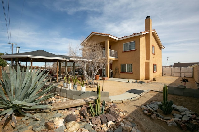 rear view of house with a chimney, stucco siding, a gazebo, fence, and a balcony