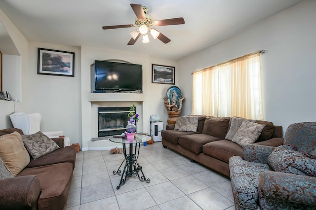living area featuring light tile patterned floors, ceiling fan, and a glass covered fireplace