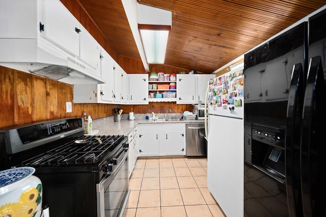 kitchen featuring stainless steel appliances, wooden walls, light tile patterned floors, white cabinetry, and lofted ceiling