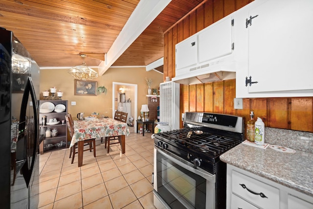 kitchen featuring black fridge, white cabinetry, wood walls, and stainless steel range with gas stovetop