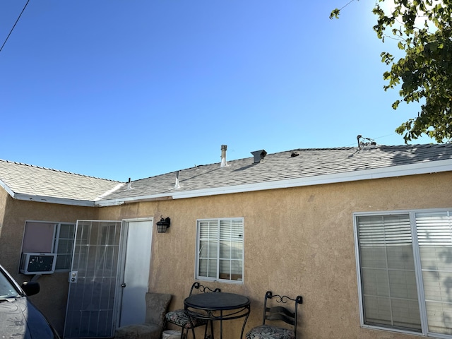 back of house with stucco siding and a shingled roof