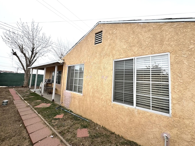 view of side of property with a patio, fence, and stucco siding