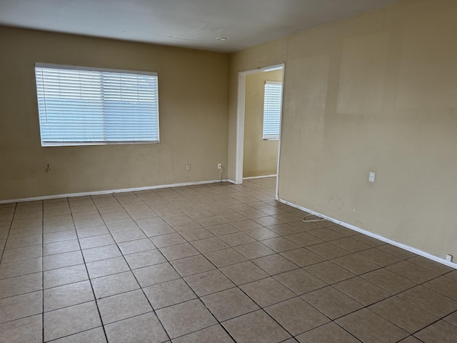 spare room with tile patterned flooring, plenty of natural light, and baseboards