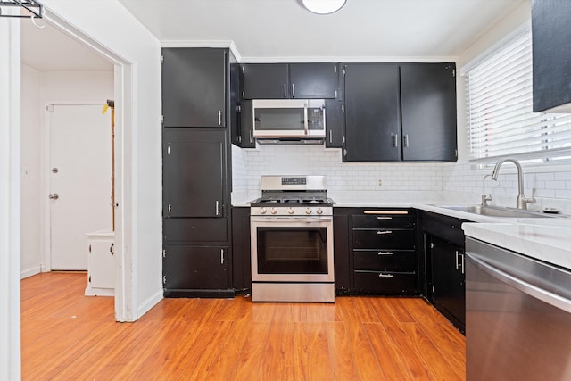 44129 Date Ave, Lancaster, CA 93534 - kitchen featuring appliances with stainless steel finishes, a sink, dark cabinets, light wood-style floors, and tasteful backsplash
