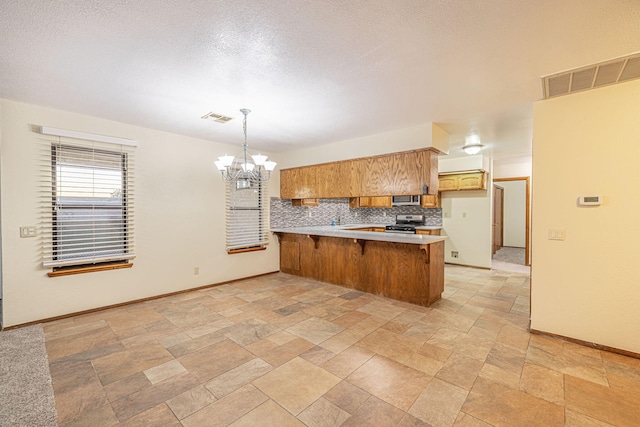 kitchen featuring an inviting chandelier, kitchen peninsula, pendant lighting, decorative backsplash, and appliances with stainless steel finishes