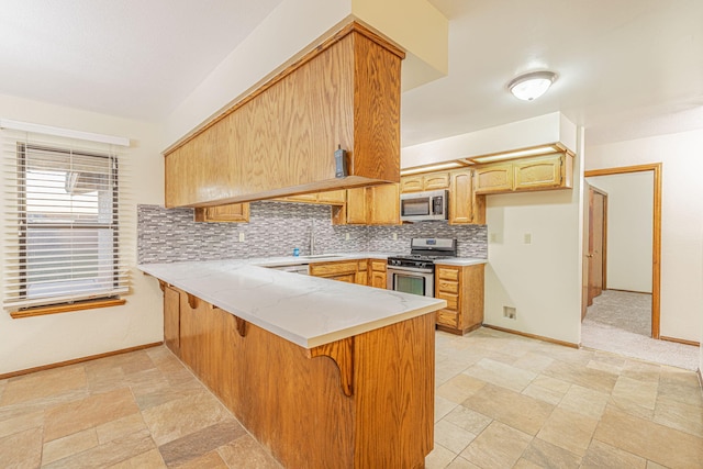 kitchen featuring kitchen peninsula, appliances with stainless steel finishes, tasteful backsplash, a breakfast bar, and sink