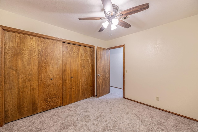 unfurnished bedroom featuring ceiling fan, a closet, light colored carpet, and a textured ceiling