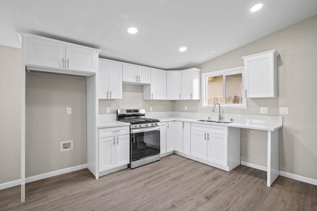kitchen featuring stainless steel range with gas stovetop, light wood-type flooring, a sink, baseboards, and white cabinets