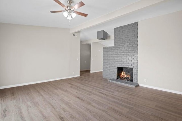 unfurnished living room featuring a fireplace, a ceiling fan, baseboards, wood finished floors, and beamed ceiling