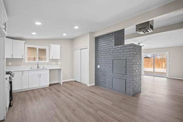 kitchen with stainless steel range with gas stovetop, a sink, light wood finished floors, and white cabinets